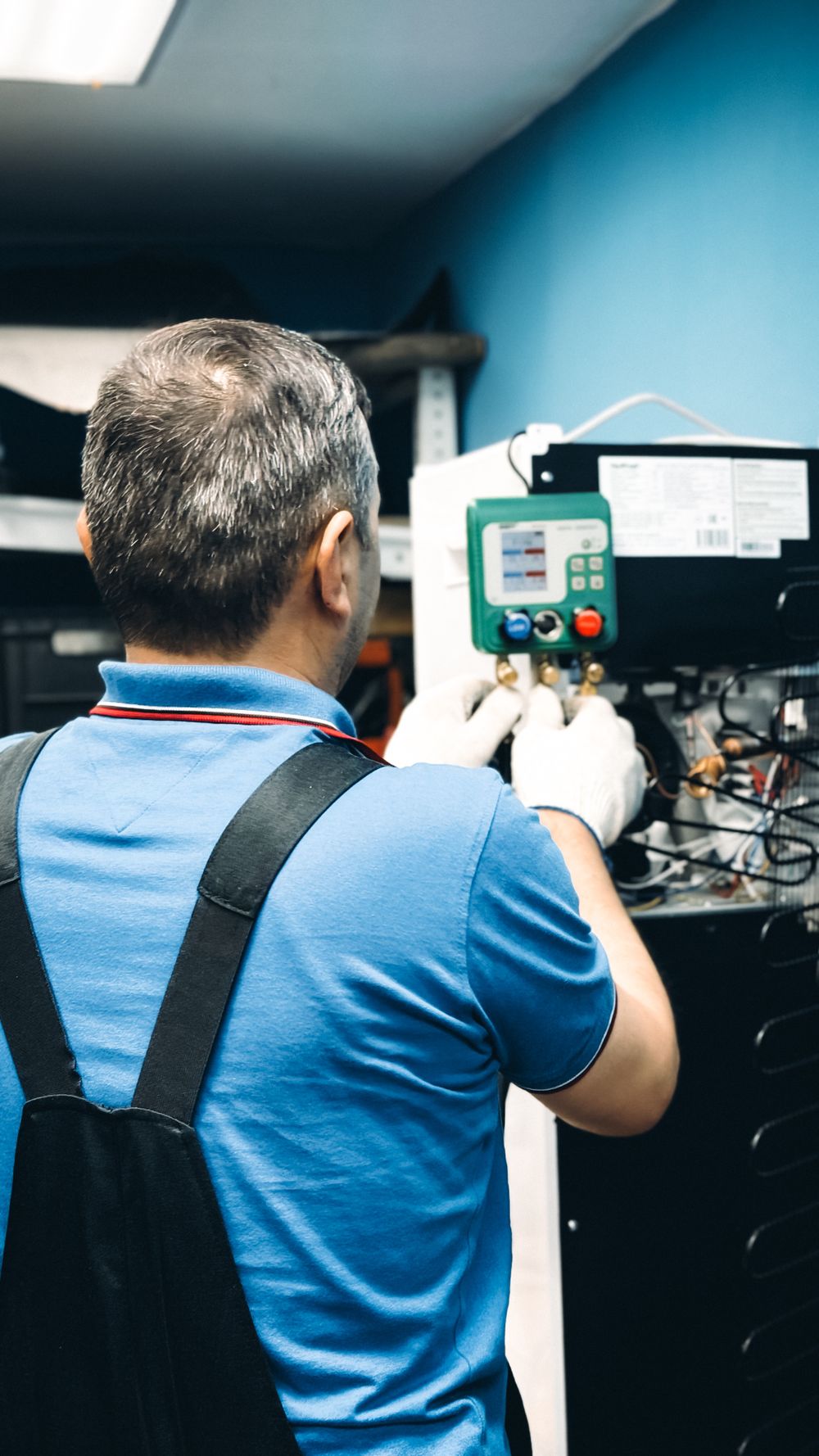 Technician servicing an indoor HVAC unit with a digital manifold